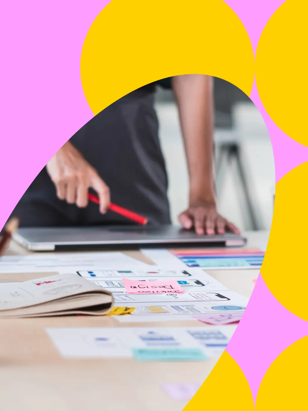 Hands at a desk with laptop, sketches, and planning materials